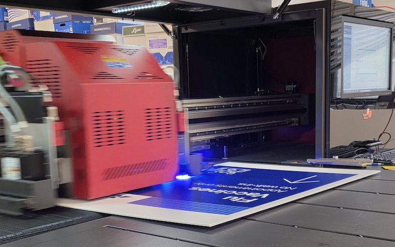 A close-up of a printing machine in action, featuring a red component and blue light as it prints on a sheet.