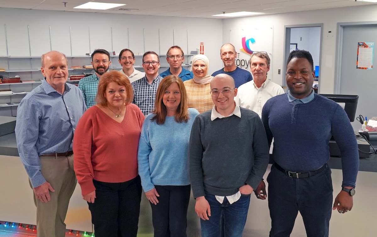 Thirteen Copytech staff members smile at the camera in a room with white walls and a service desk.
