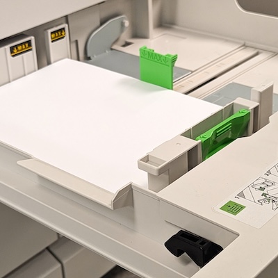 Printer section with white paper secured by green tabs inside the tray.