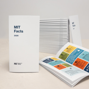 Stack of MIT Facts 2026 booklets displayed on a neutral surface, with one upright booklet showing a white cover labeled “MIT Facts 2026” in blue text, several copies fanned out behind it, and an open booklet in the foreground revealing colorful, multi-section pages with icons and data blocks.
