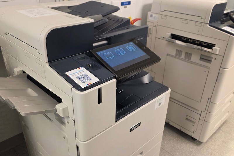 Close-up of a modern office printer with a touchscreen interface showing printing options.